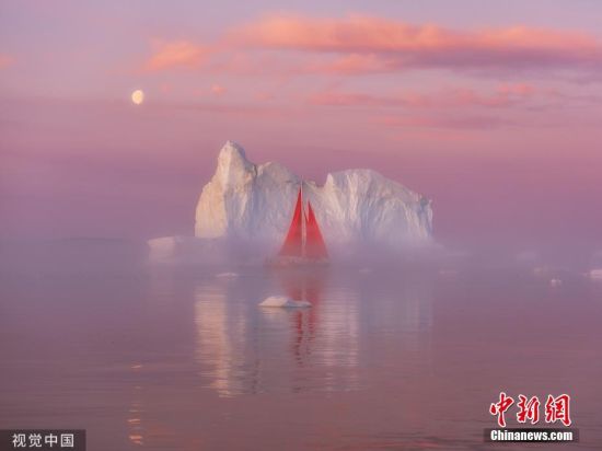 9月5日讯(具体拍摄时间不详)，格陵兰岛迪斯科湾，一艘挂着红帆的游艇在形状各异的冰山之间航行，为宁静的北极夜晚增添了一抹亮色。图片来源：视觉中国